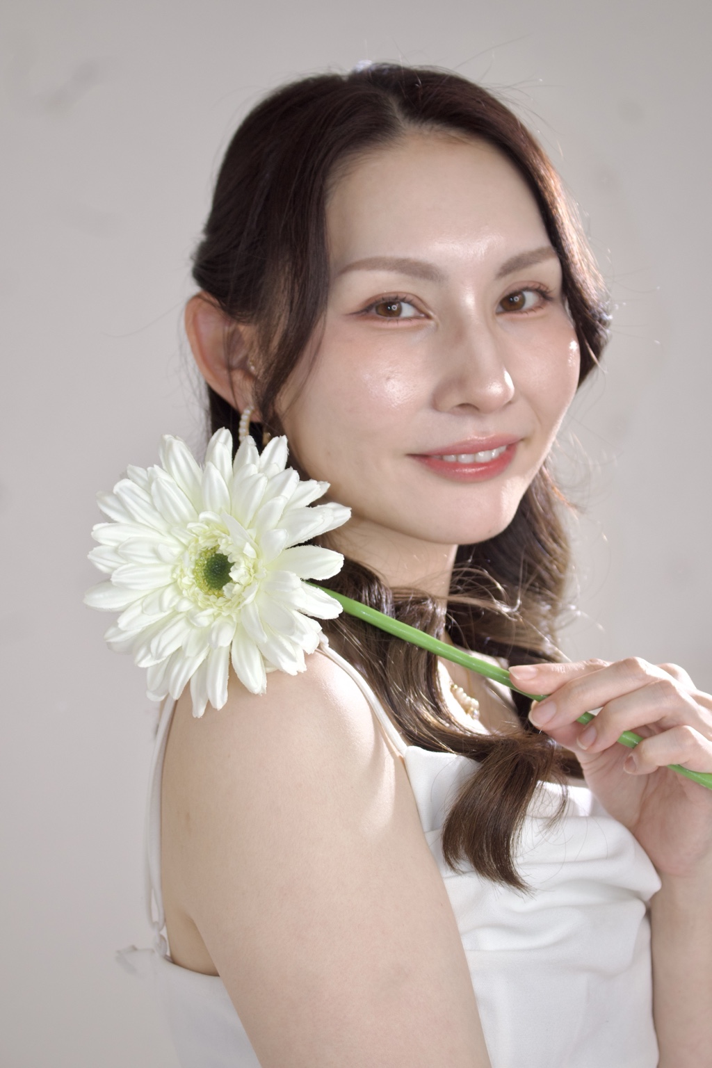 白いガーベラを手に微笑むMeg.Lipアーティスト 歯科衛生士さが